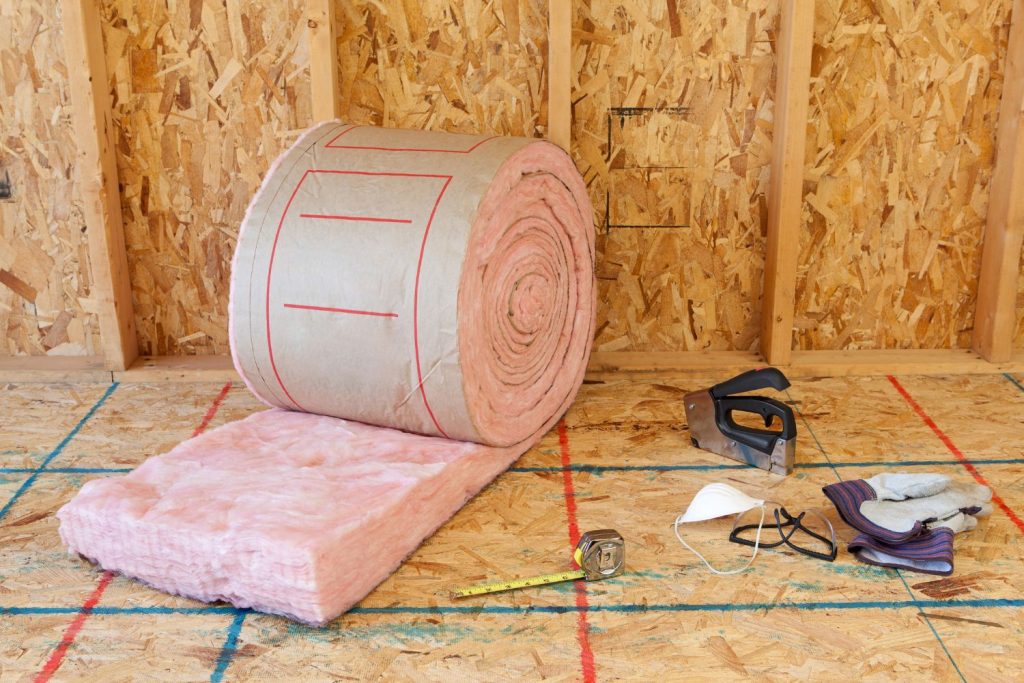A roll of pink insulation material is placed on the floor, showcasing its soft texture and vibrant color.